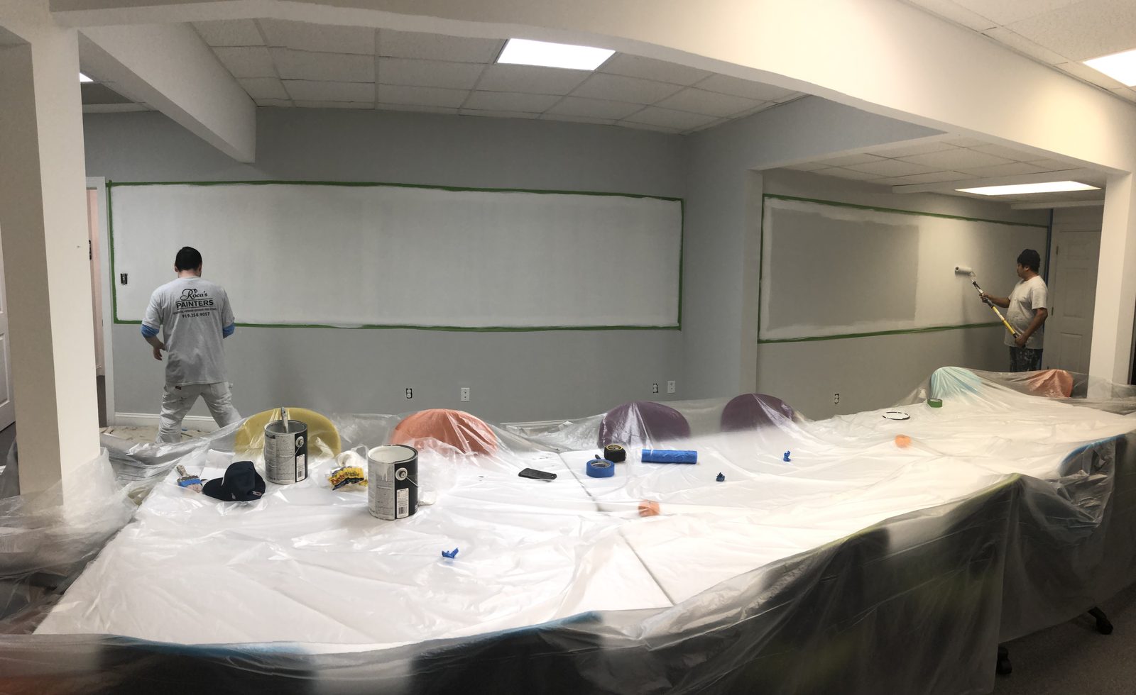 Two painters applying dry-erase coating to a large conference room wall